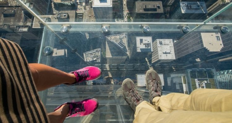 Two people looking down at their feet and Chicago streets from the Skydeck at Willis Tower